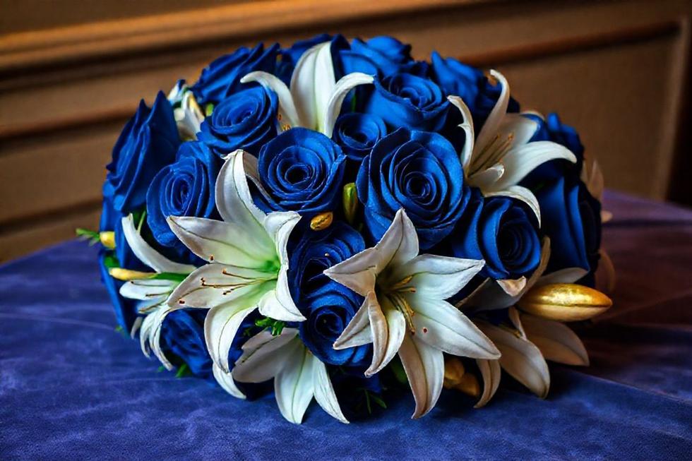 Buquê sofisticado com rosas azul royal, lírios brancos e detalhes dourados, representando luxo acessível.
